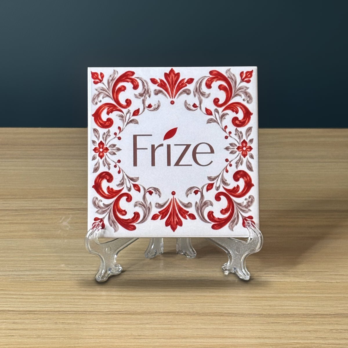 Azulejo blanc avec le logo de l'entreprise Frize dans une bordure baroque rouge et grise, sur un support transparent.